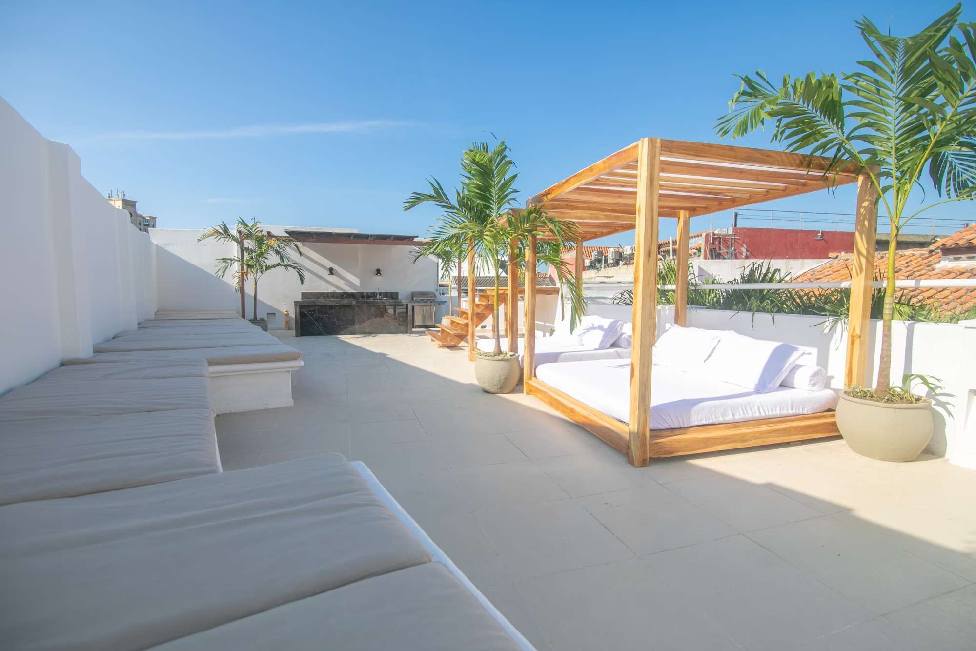 Terraço no telhado com uma cama de madeira, espreguiçadeiras brancas e plantas em vasos.