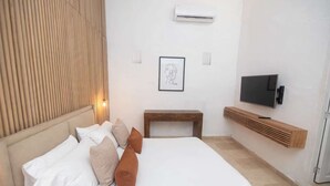 Ein Schlafzimmer mit einem Bett, Kissen, einem Nachttisch, einem Fernseher und einer Klimaanlage.