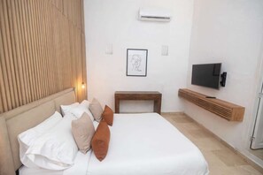 A bedroom with a bed, pillows, a bedside table, a TV, and an air conditioning unit. - Luxury Room in Casa Escallon (Cartagena)