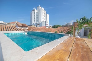 A rooftop swimming pool with a wooden deck, surrounded by buildings with red-tiled roofs. - Luxury Room in Casa Escallon (Cartagena)