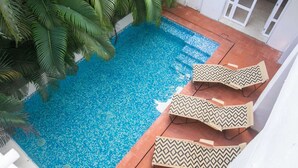 Ein Schwimmbecken mit einem gemusterten Fliesenboden, umgeben von Palmen und einem weißen Gebäude.
