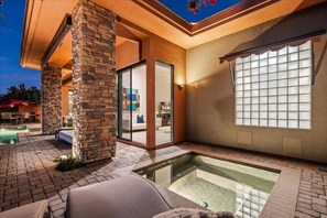 Um pátio moderno ao ar livre com piscina, pilares de pedra e porta de vidro que dá para um espaço interno.