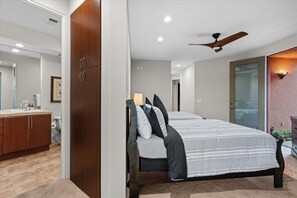 Quarto com cama, ventilador de teto e banheiro visível ao fundo.