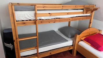 Ein Etagenbett mit Holzrahmen, grau-weißer Bettwäsche und einem roten Kopfkissen.