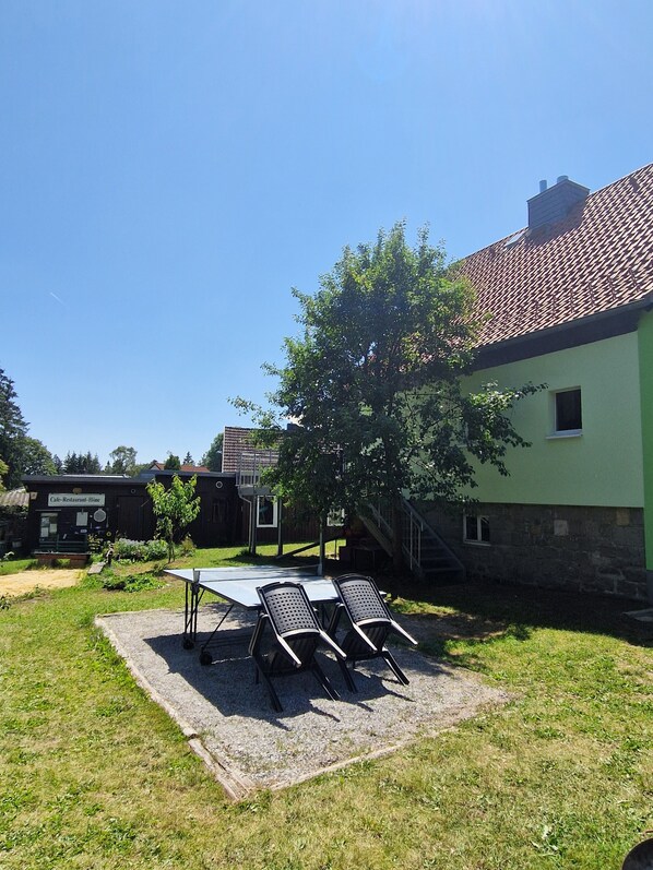 An outdoor seating area with a table and chairs, a building with a green facade, and a tree.