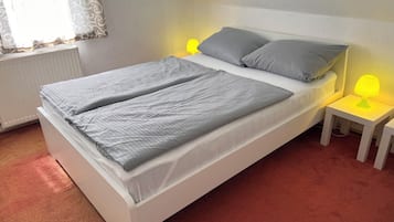 Una cama con dos almohadas, una mesita de noche con una lámpara y una ventana con cortinas.