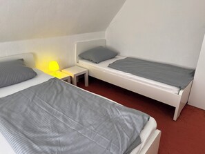 Habitació amb dos llits, una taula petita i una làmpada.