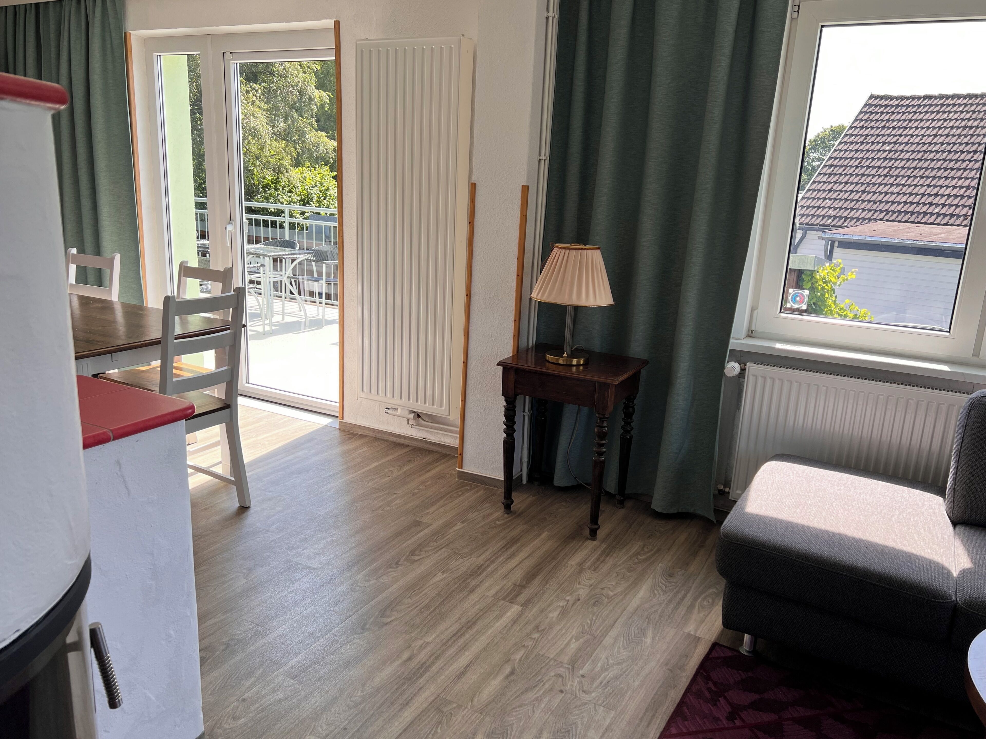 Ein Zimmer mit Esstisch, Stühlen, einer Lampe, einem Sofa und Blick durch ein Fenster.