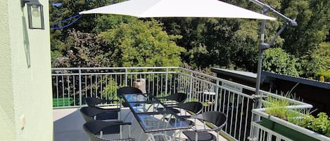 An outdoor patio with a table and chairs, a white umbrella, and a railing.
