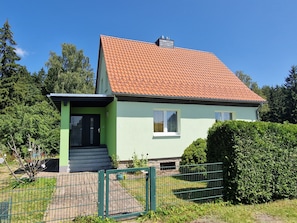 A two-story house with a red-tiled roof, a green door, and a small front porch.