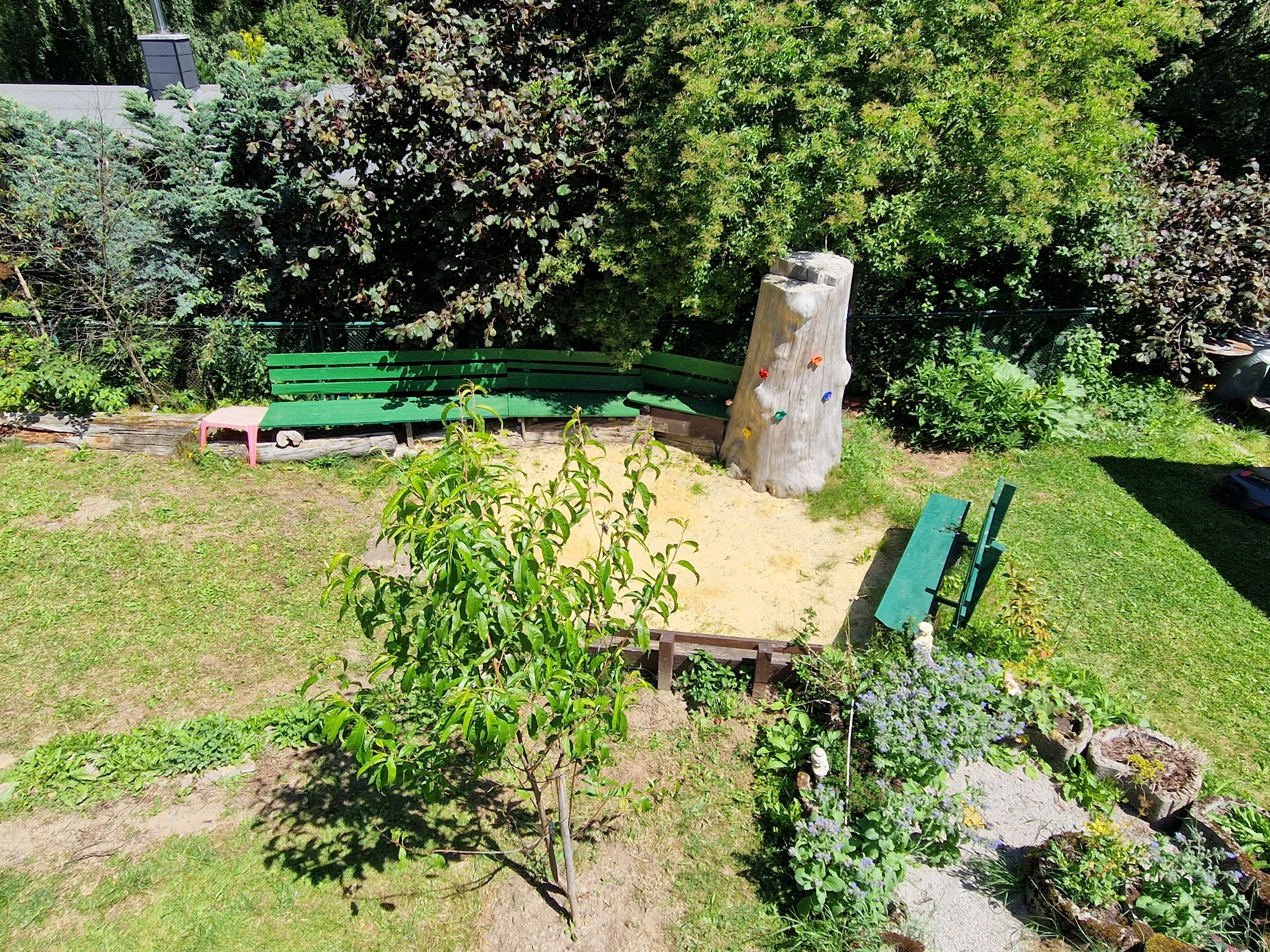 Ein Park mit grünen Bänken, einem Kletterbaum und einer Sandfläche.