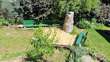 Ein Park mit grünen Bänken, einem Kletterbaum und einer Sandfläche.