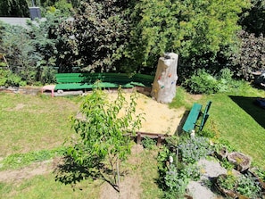 A park with green benches, a climbing tree, and a sandy area.