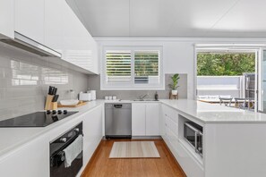 A modern kitchen with white cabinetry, a dishwasher, a stove, and a window with blinds. - Orara Oasis - Close to Beaches | 4Pines Park | Shopping | Breweries (Allambie Heights)