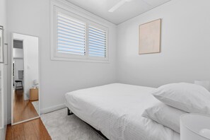 Ein Schlafzimmer mit einem Bett, einem Fenster mit Jalousien, einer Tür und einem an der Wand befestigten Kunstwerk.