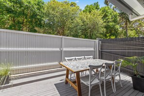 Eine Terrasse mit Tisch und Stühlen, umgeben von einem Holenzaun und viel Grün.