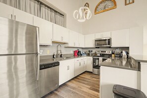 A modern kitchen with stainless steel appliances, white cabinetry, and a wooden floor. - New Stylish Indy Apt- Perfect for Groups - 3BR (Indianapolis)