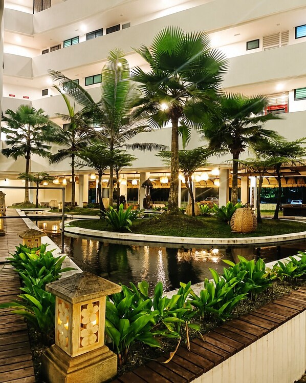 A hotel lobby with a central water feature, surrounded by palm trees and plants.