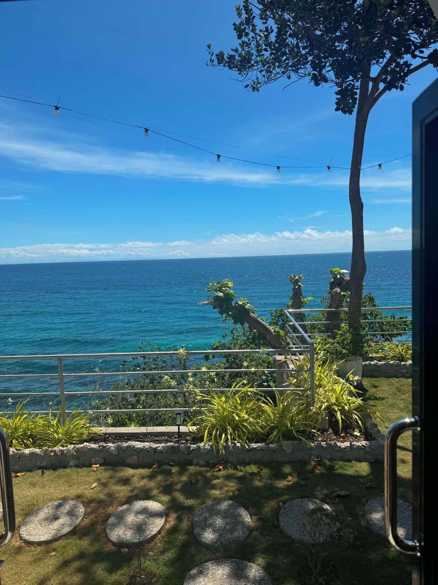 A coastal view with a railing, greenery, and a clear sky.
