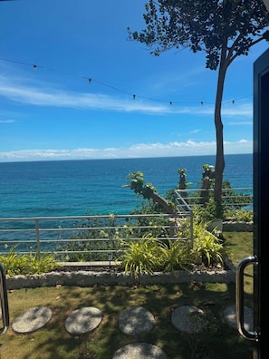 Vista costera con barandilla, vegetación y cielo despejado.
