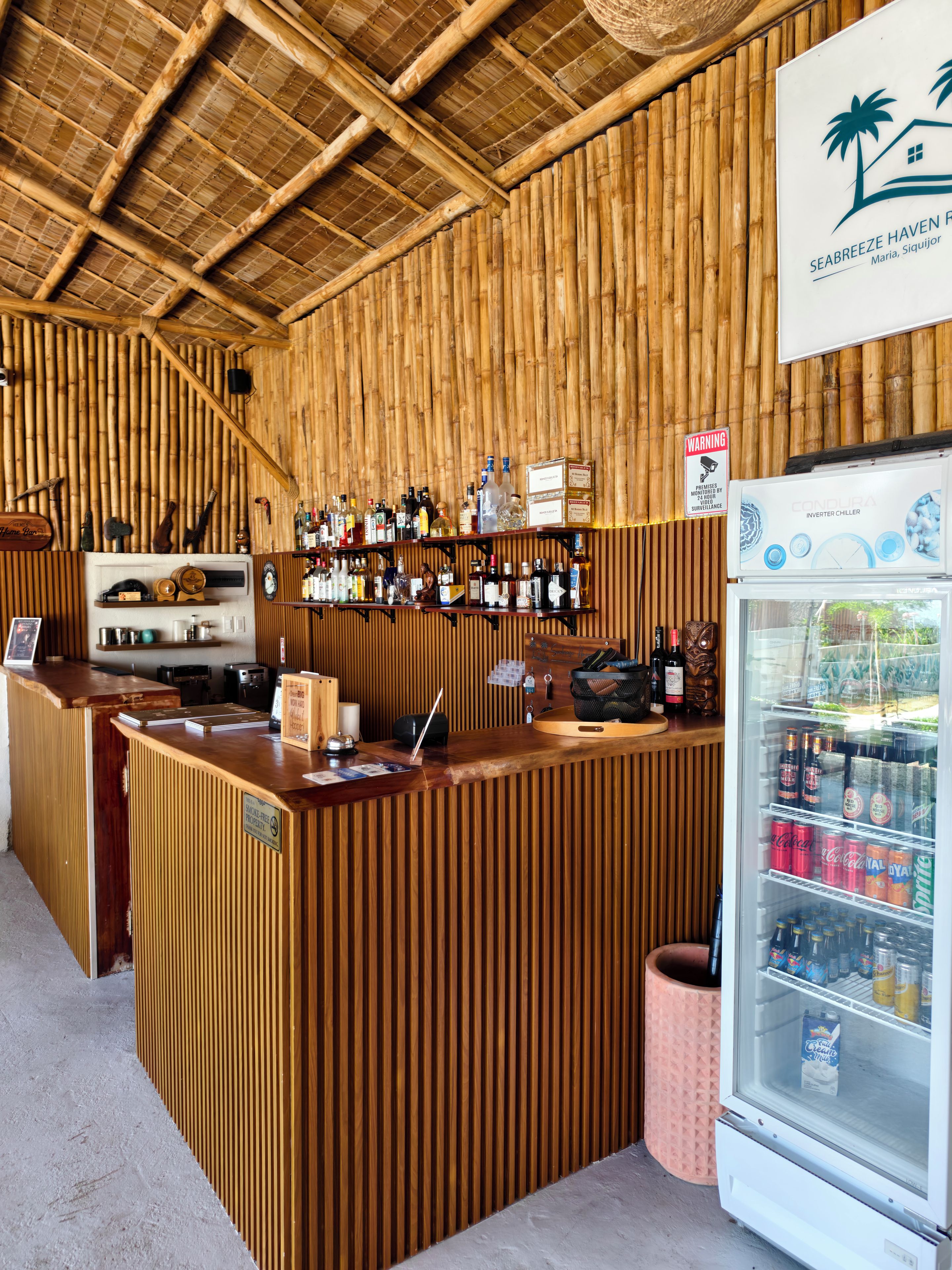 A bar area with a bamboo wall, wooden counter, and a refrigerator stocked with beverages.