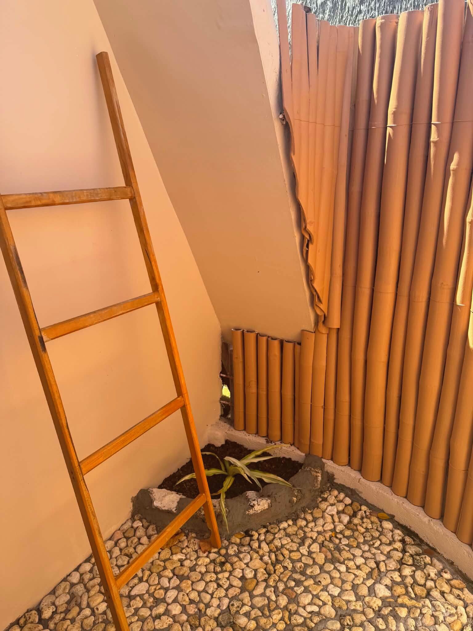 Eine Ecke mit einer Holzleiter, einem Bambuszaun und einem Boden mit Kieselsteinen.