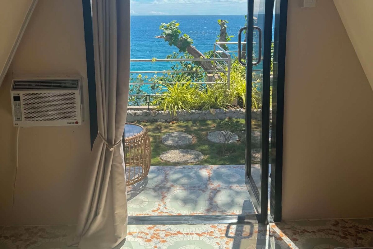 A room with a view of the sea, a window with curtains, a radiator, and a patterned floor.