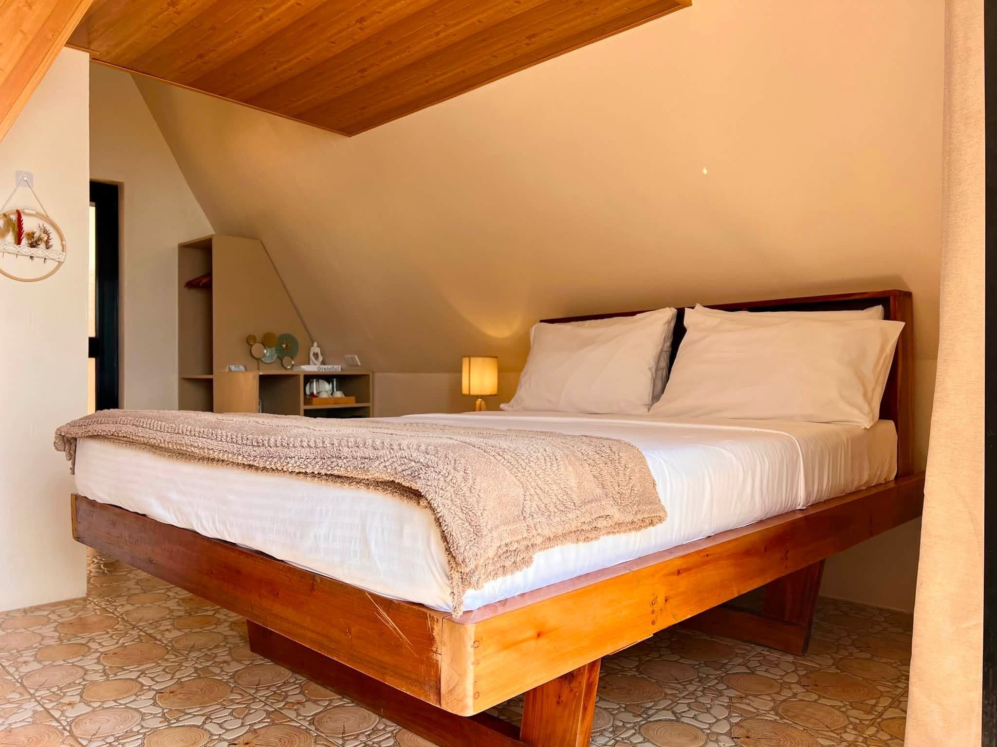 A single bed with a wooden frame and white bedding in a room with a sloped ceiling and stone-patterned floor.