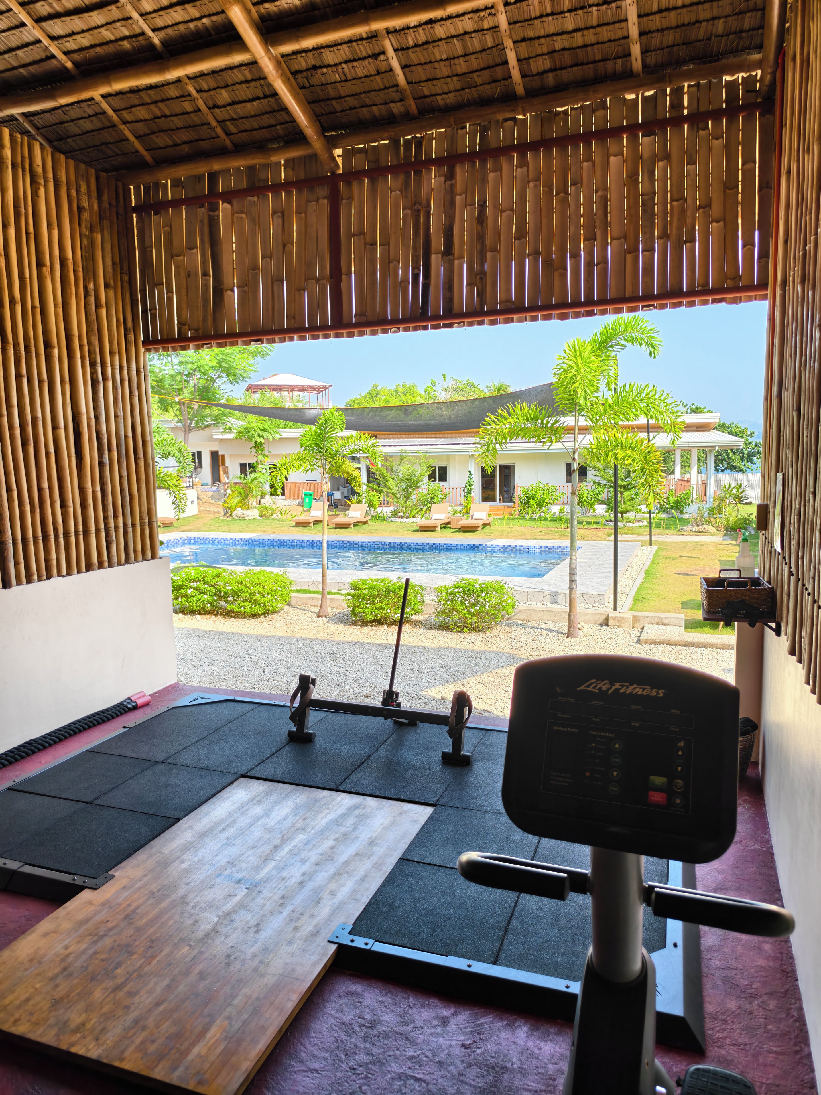 An indoor gym with exercise equipment, a view of a pool, and a building in the background.