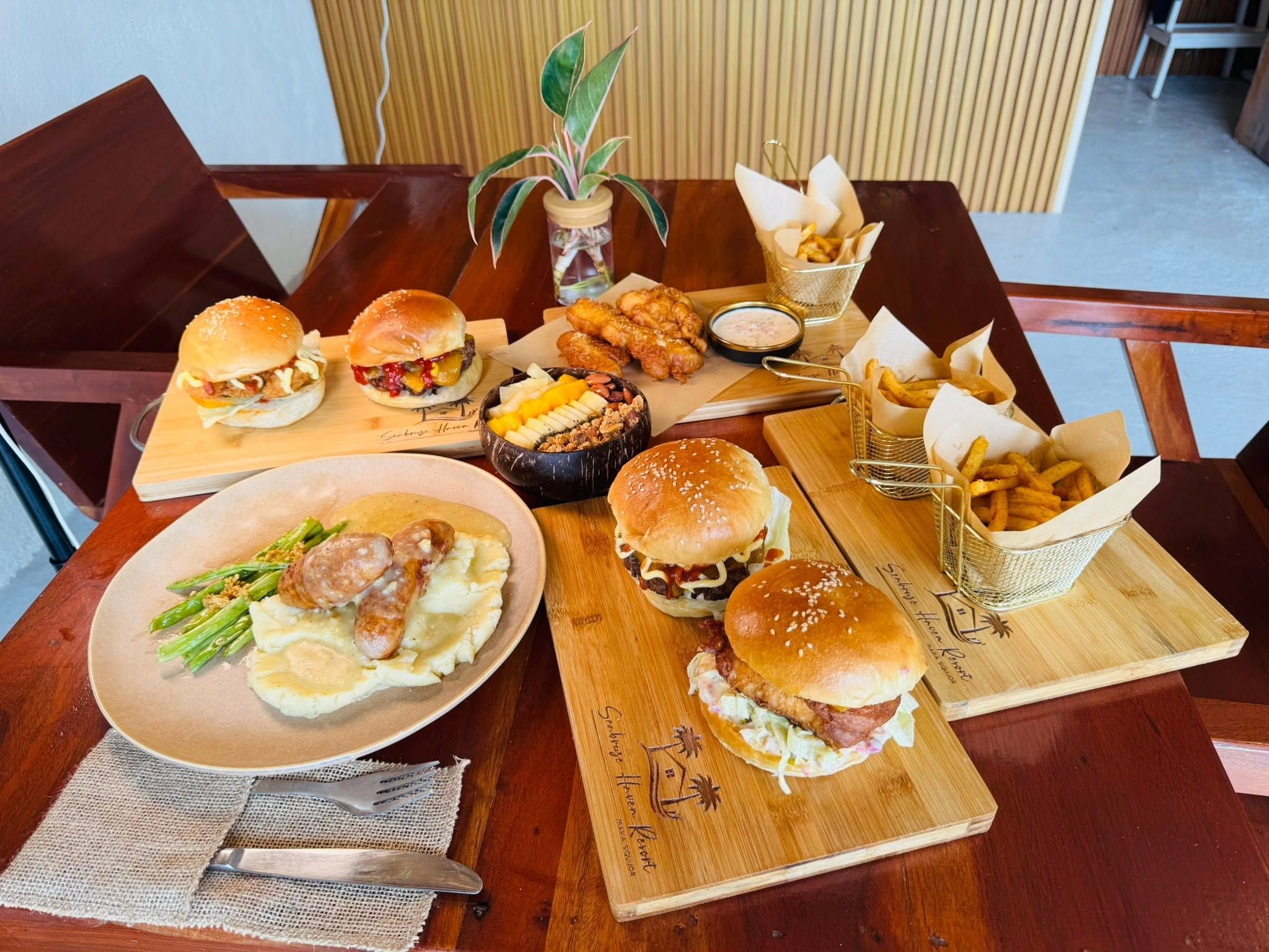 Ein Holztisch mit verschiedenen Speisen, darunter Burger, Pommes und eine Salatschüssel.