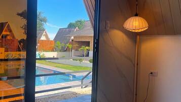 A room with a sliding glass door leading to a pool area, a small potted plant on a white table, and a floor lamp.