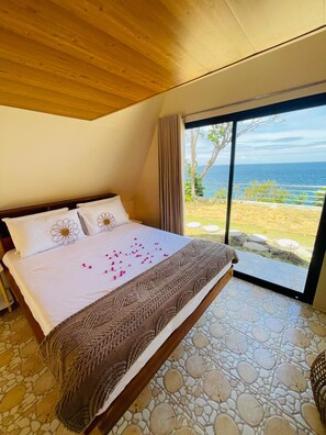 A bedroom with a large bed, a view of the sea, and a stone floor. - Seabreeze Haven Resort (Maria)