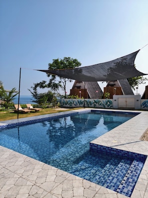 A swimming pool with tiled edges, lounge chairs, and a shaded area with a unique architectural design. - Seabreeze Haven Resort (Maria)