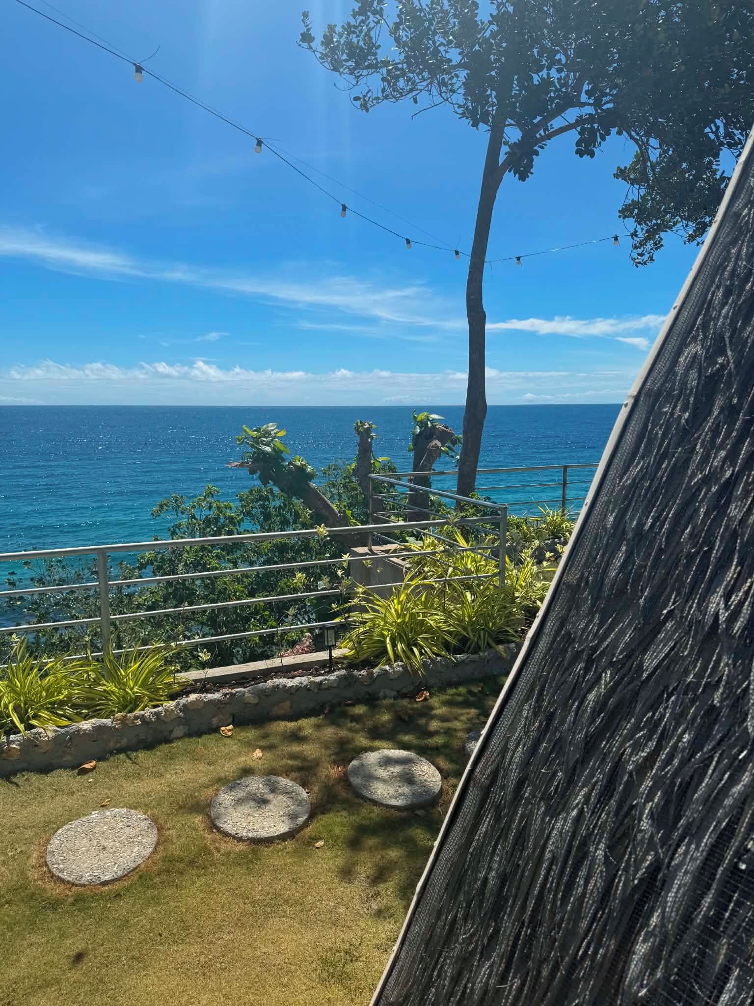 A coastal view with a railing, greenery, and a clear sky.