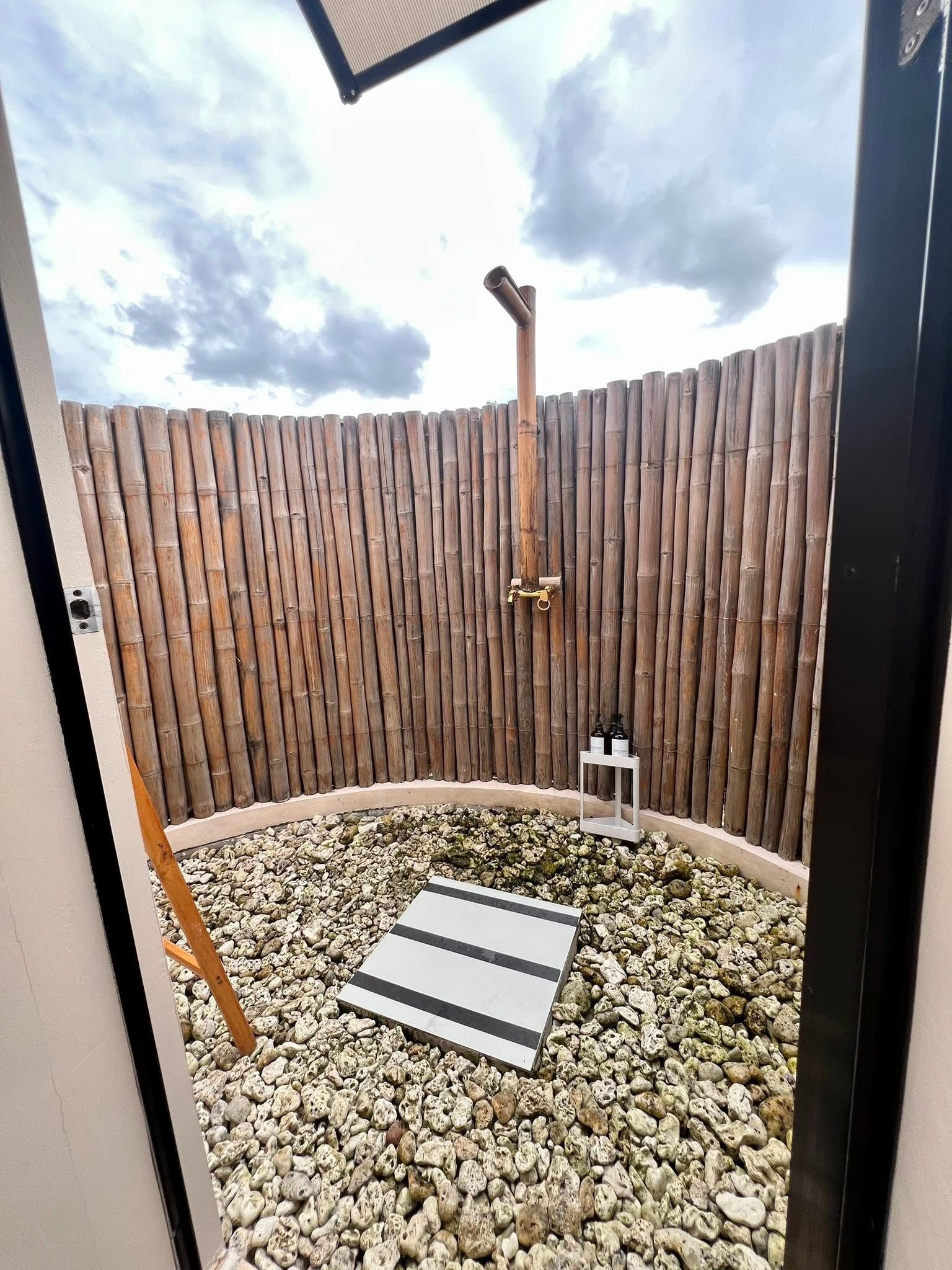 A small outdoor area with a bamboo fence, a showerhead, and a tiled floor.