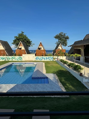 A pool area with a clear view of the sea, surrounded by three bungalow-style buildings with a tropical design. - Seabreeze Haven Resort (Maria)