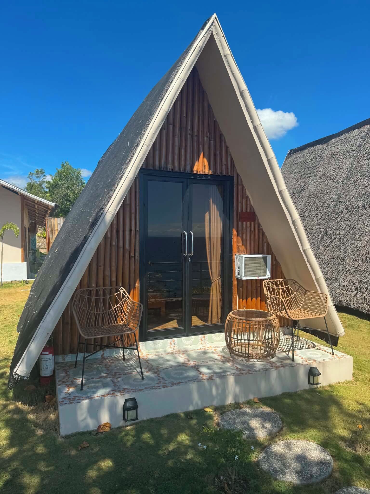 A triangular building with a glass door entrance, two wicker chairs, and a small table.