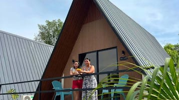 Un moderno edificio tipo cabaña con balcón, mobiliario exterior y cielo despejado.