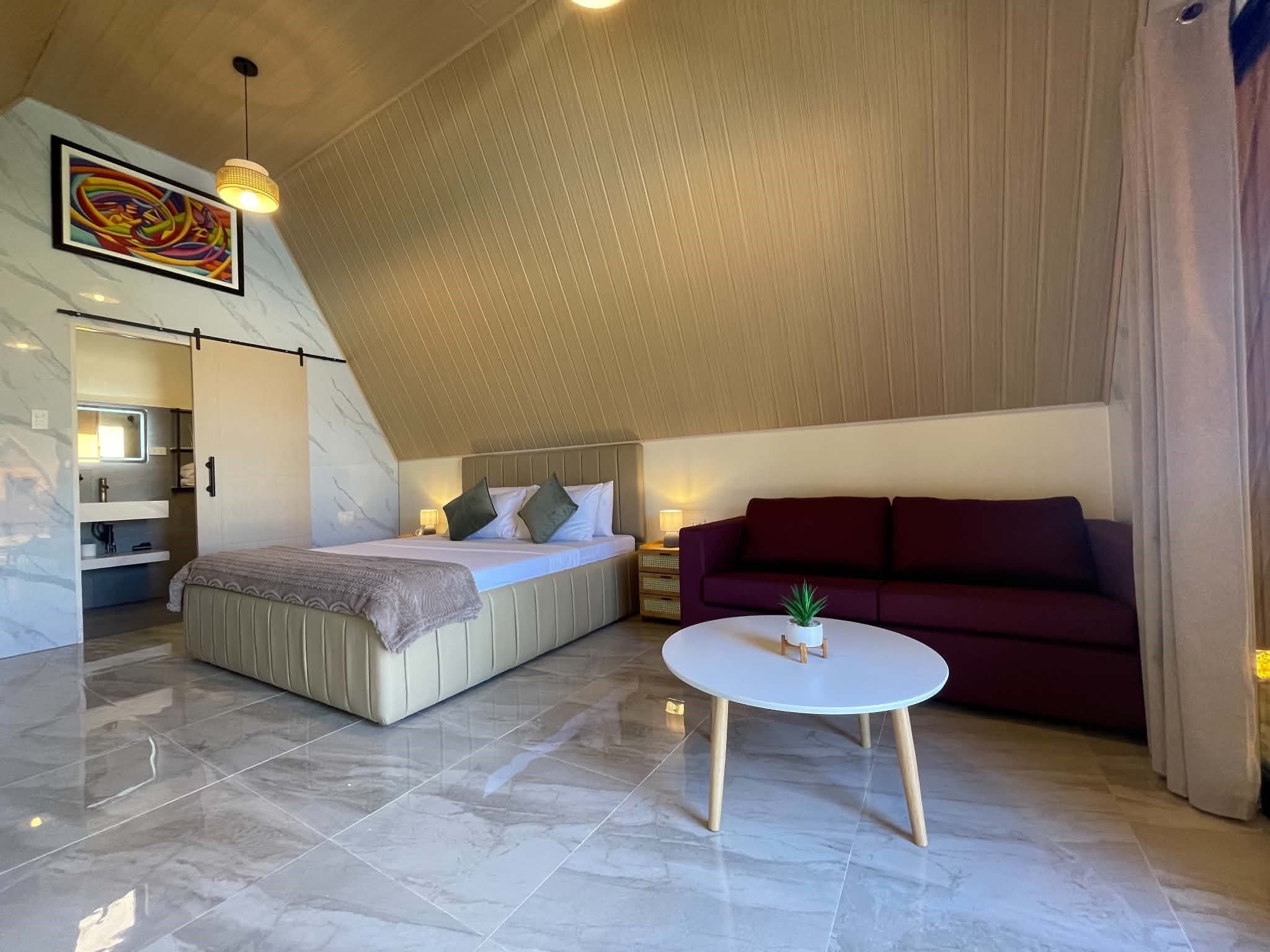 A modern loft bedroom with a large bed, a sofa, a small table, and a ceiling with a sloped design.