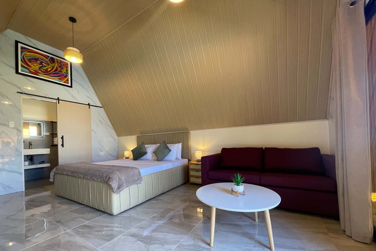A modern bedroom with a bed, a sofa, a small table, and a ceiling with a sloped design.