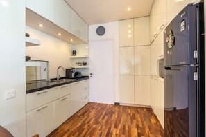 A modern kitchen with white cabinets, a black refrigerator, and a wooden floor. - Private Pool | Garden Lounge | Dedicated Workspace (Canggu)