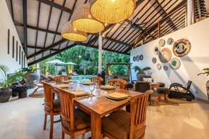 A dining area with a wooden table set for four, surrounded by chairs, under a high ceiling with woven light fixtures. - Private Pool | Garden Lounge | Dedicated Workspace (Canggu)