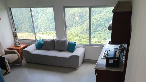 A modern living room with a sofa, a coffee table, and a view of greenery through large windows.