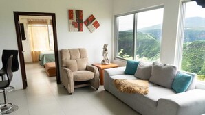 A modern living room with a sofa, armchair, and a view of a mountainous landscape through large windows.
