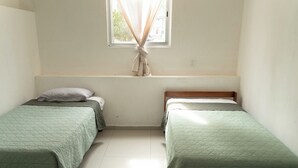 Een kamer met twee eenpersoonsbedden, een raam met gordijnen en een witte muur.