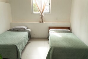 A room with two single beds, a window with curtains, and a white wall. - Vrbo Property (Tonalá)