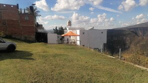 A grassy area with a white building, a red brick structure, and a white car parked on the left.