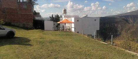 Un espacio cubierto de césped con un edificio blanco, una construcción de ladrillo rojo y un coche blanco estacionado a la izquierda.