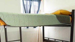 Een stapelbed met een ladder, een raam met blauwe gordijnen en een houten nachtkastje.