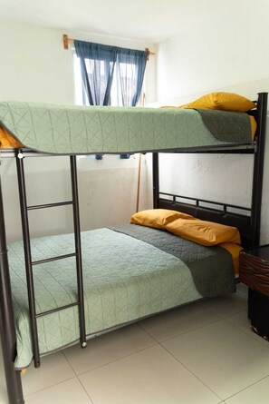 A bunk bed with a ladder, a window with blue curtains, and a wooden nightstand. - Vrbo Property (Tonalá)